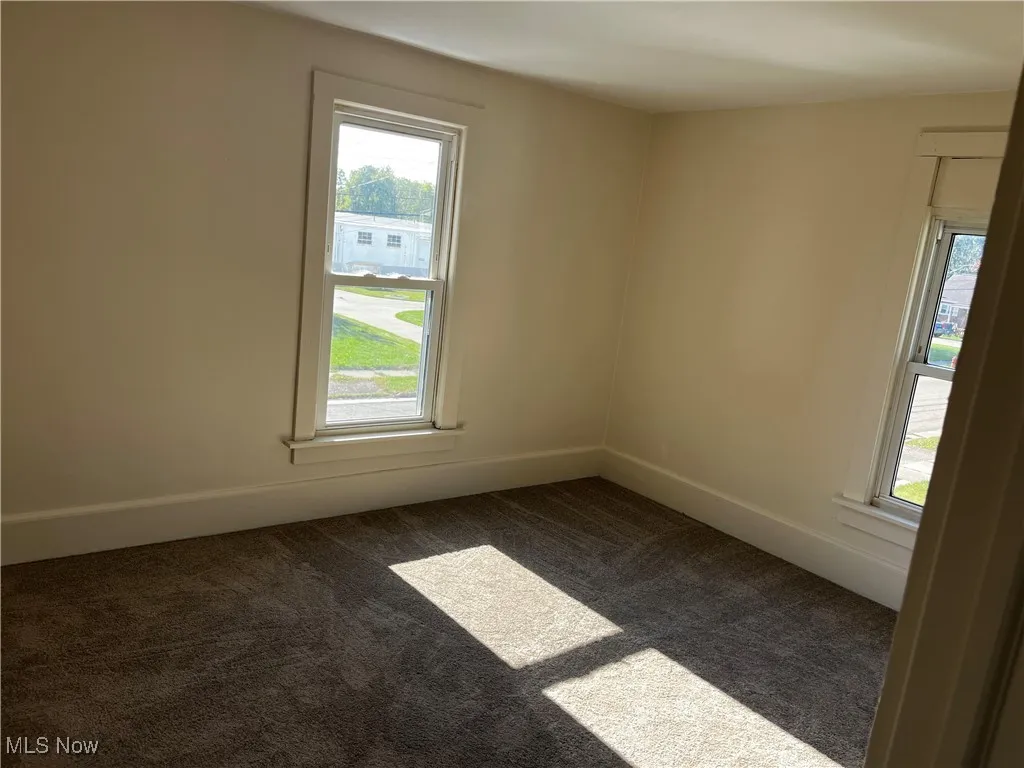 Unfurnished room featuring dark colored carpet and baseboards
