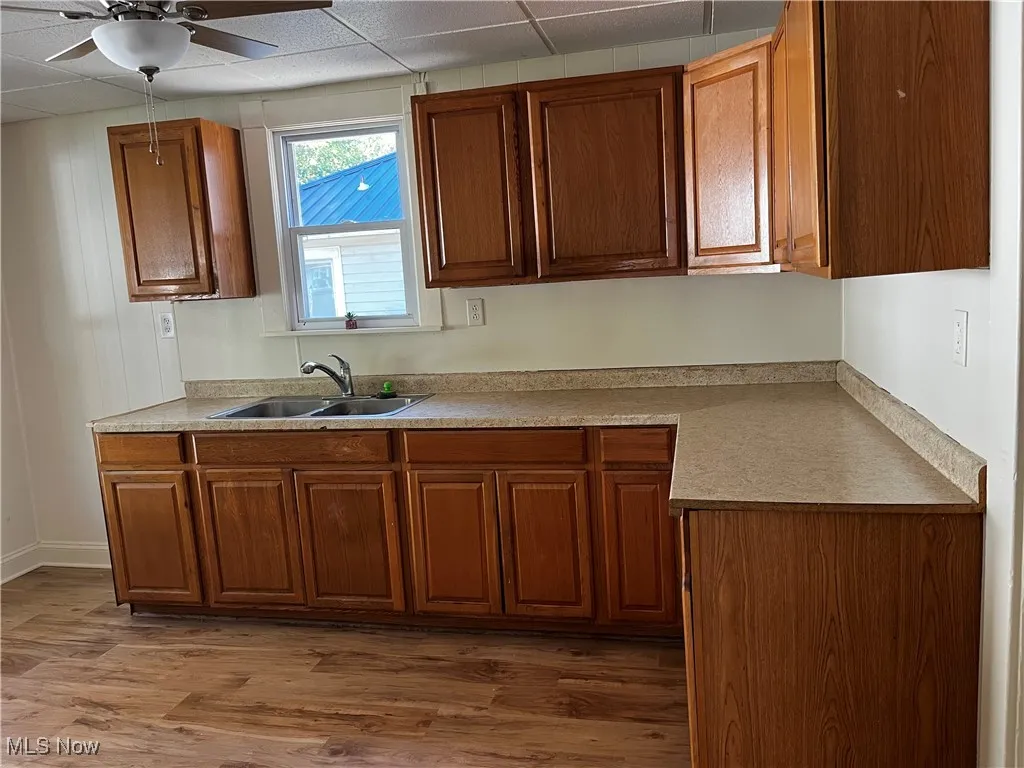 Kitchen featuring light countertops, dark wood-style flooring, brown cabinets, a drop ceiling, and ceiling fan