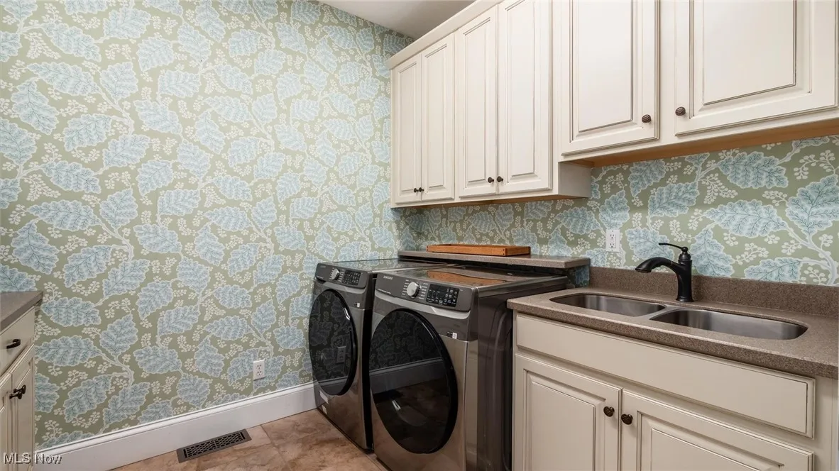 Laundry area featuring wallpapered walls, washer and clothes dryer, cabinet space, and light tile patterned floors