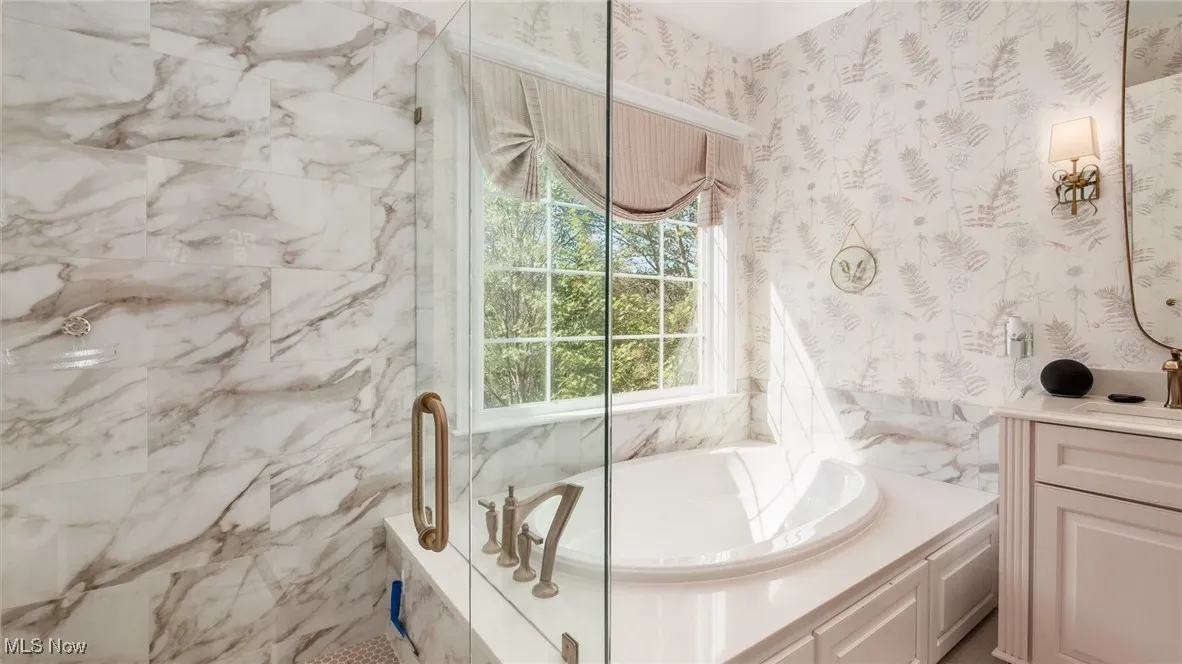 Bathroom featuring wallpapered walls, a garden tub, vanity, and a marble finish shower