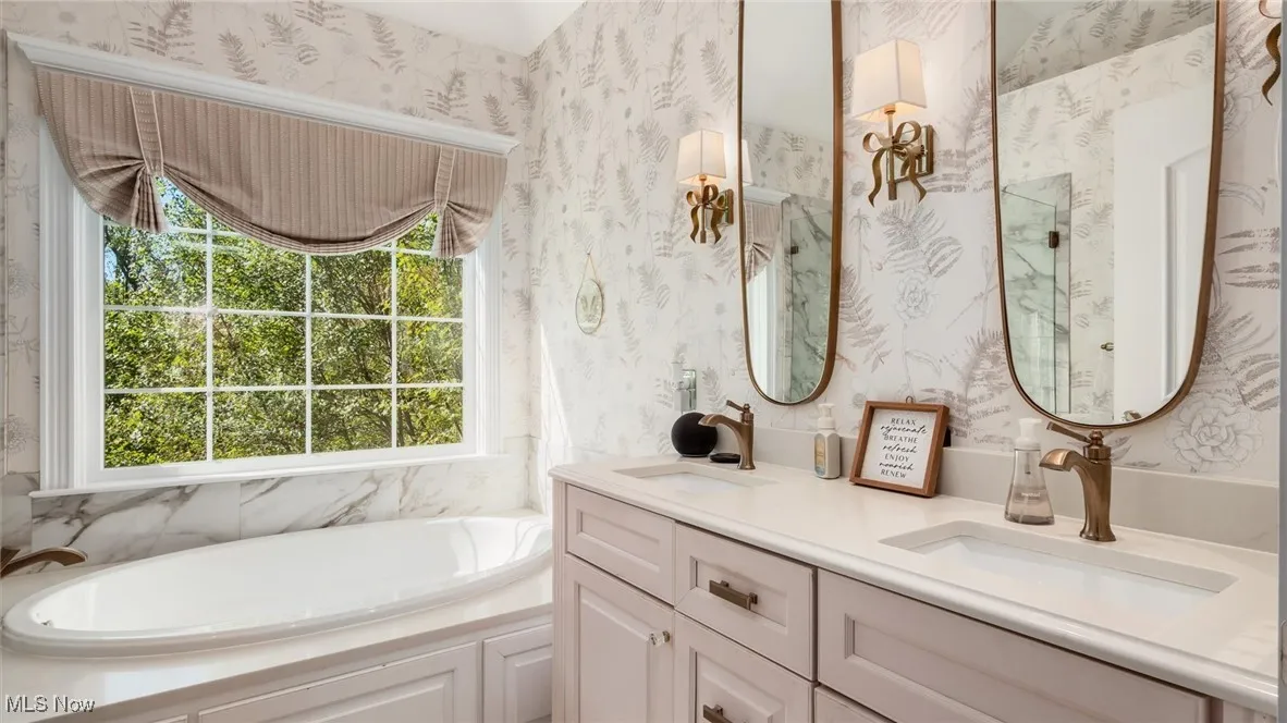 Bathroom featuring a garden tub, double vanity, and wallpapered walls