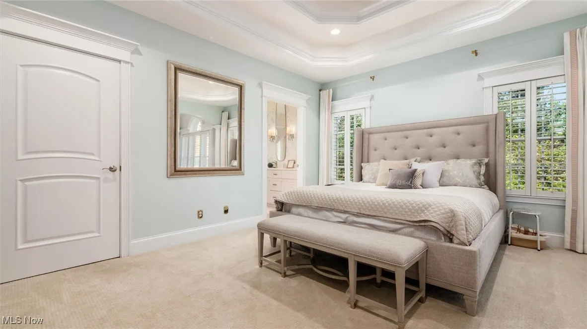 Carpeted bedroom with multiple windows, connected bathroom, crown molding, a raised ceiling, and recessed lighting