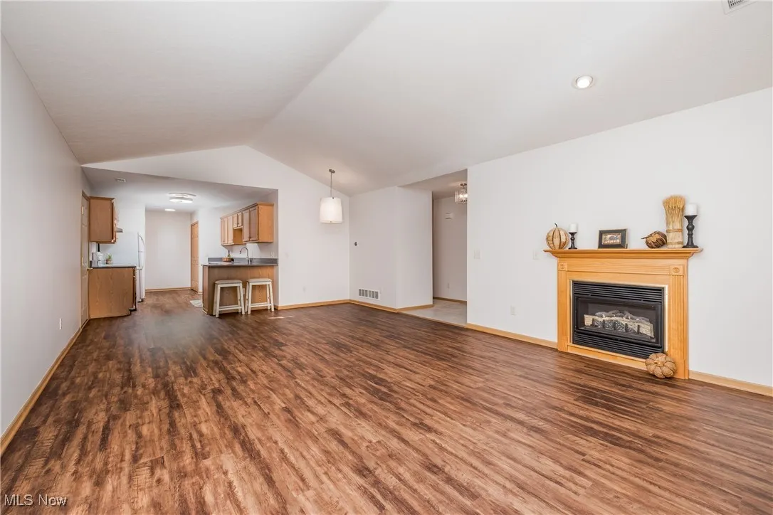 Unfurnished living room featuring a glass covered fireplace, dark wood-style flooring, vaulted ceiling.