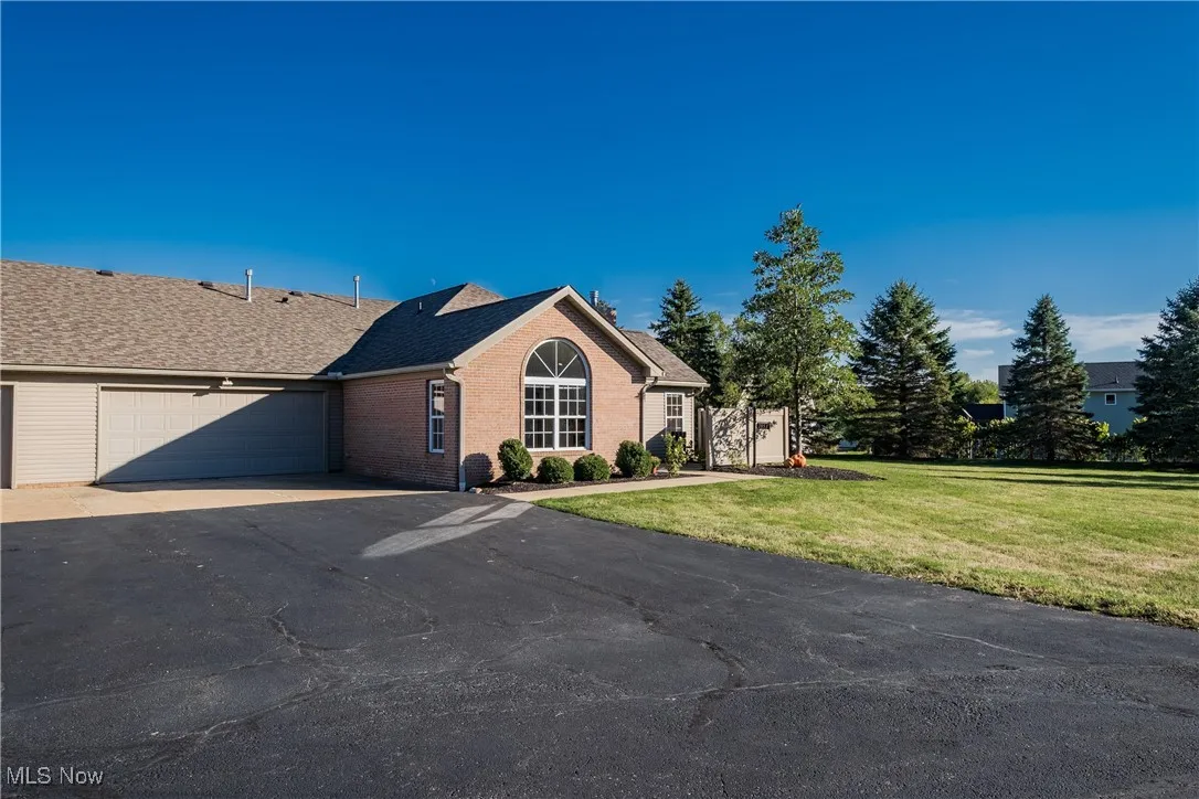 Ranch-style home featuring a front lawn, asphalt driveway, brick siding, an attached garage, and roof with shingles