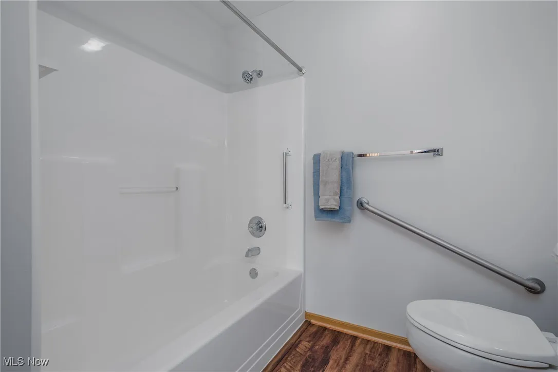 Bathroom with dark wood-style flooring and shower / tub combination