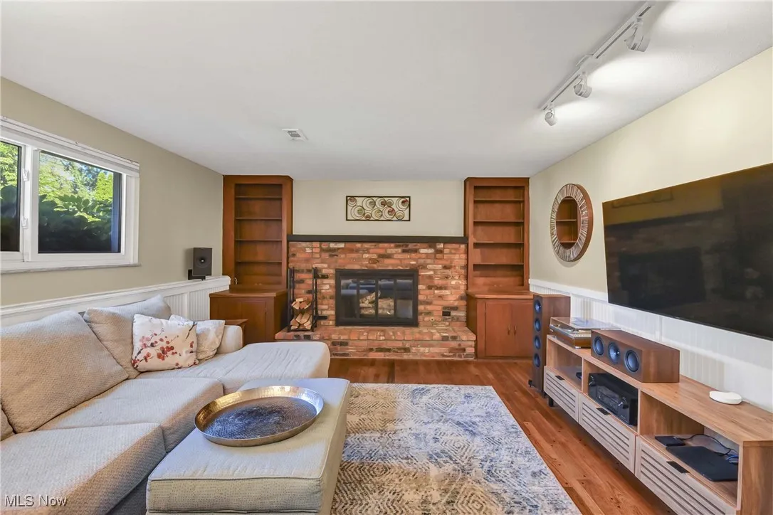 Living area with built in features, a wainscoted wall, wood finished floors, a fireplace, and rail lighting