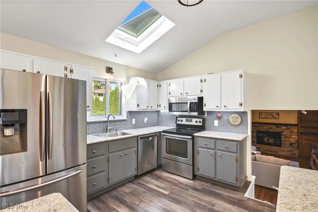 Kitchen featuring stainless steel appliances, gray cabinetry, white cabinetry, lofted ceiling, and dark wood-style floors