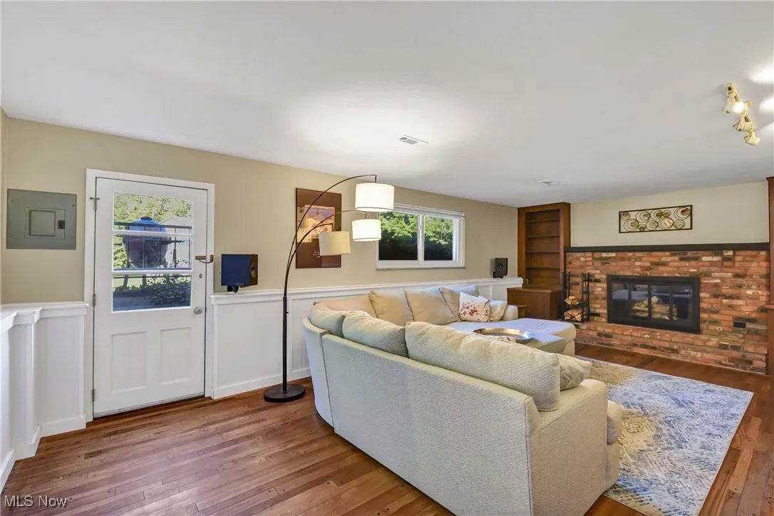 Living area with electric panel, wood-type flooring, a brick fireplace, and wainscoting