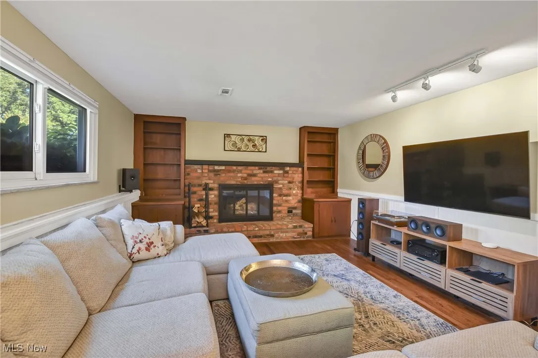 Living room featuring built in shelves, wood finished floors, a fireplace, a wainscoted wall, and rail lighting
