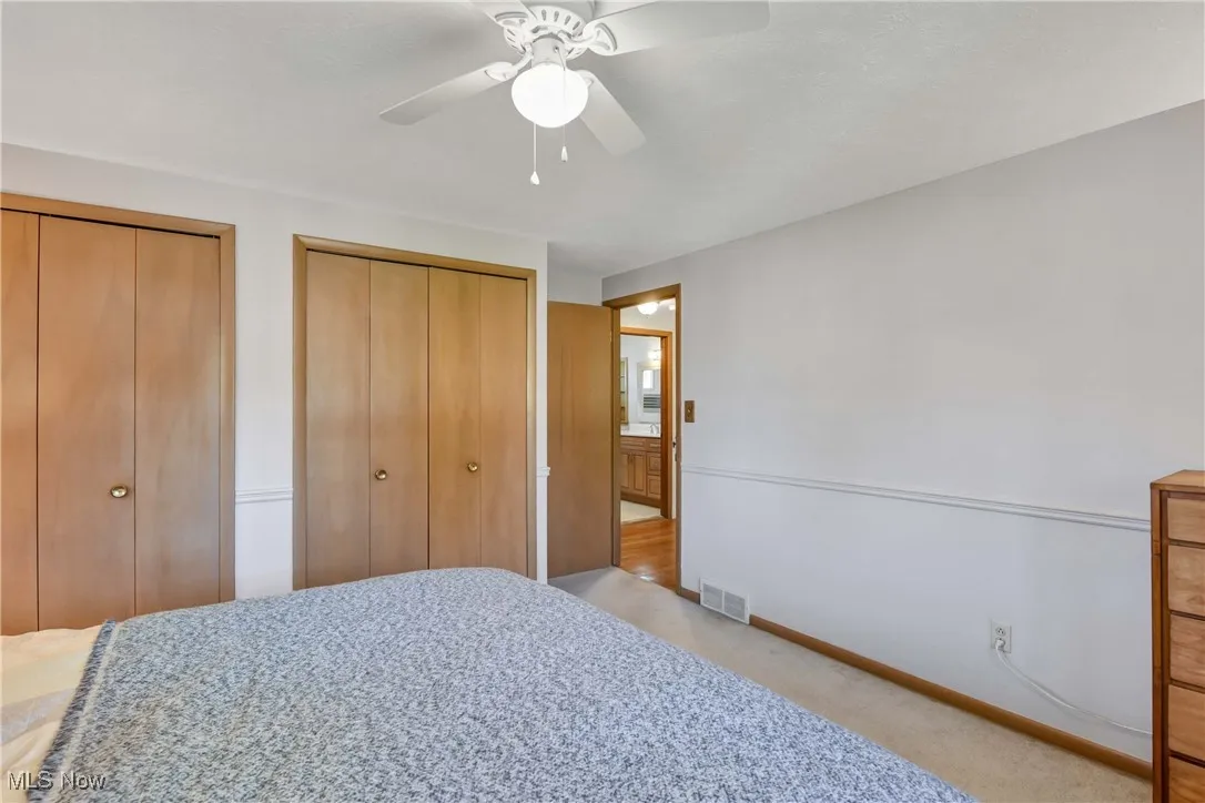 Bedroom with two closets, light carpet, and a ceiling fan