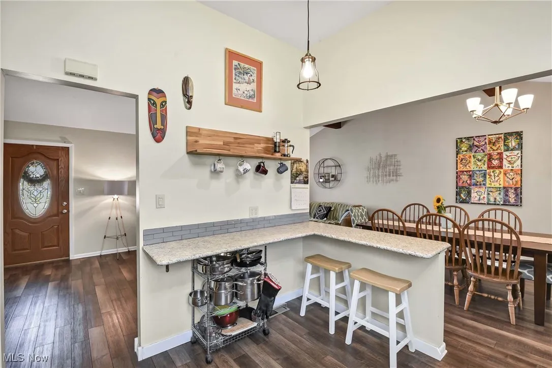 Kitchen featuring a breakfast bar, dark wood finished floors, open shelves, a peninsula, and a towering ceiling