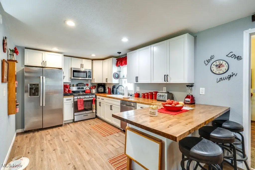 Kitchen with appliances with stainless steel finishes, a breakfast bar, a peninsula, pendant lighting, and light wood-style flooring