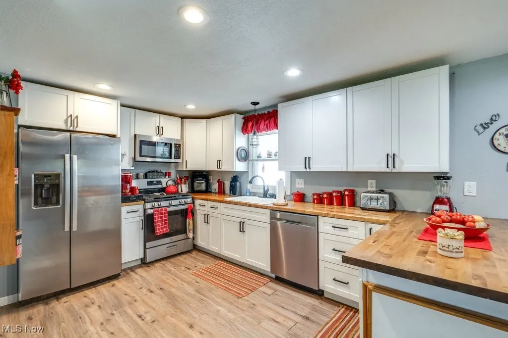 Kitchen featuring stainless steel appliances, white cabinets, pendant lighting, butcher block counters, and light wood-style floors