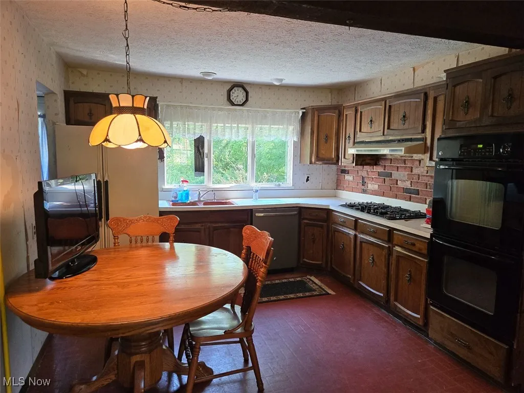 Kitchen featuring wallpapered walls, stainless steel appliances, light countertops, a textured ceiling, and under cabinet range hood