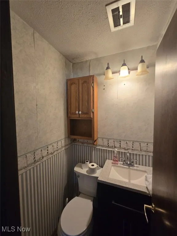 Bathroom with vanity, a textured ceiling, and wallpapered walls
