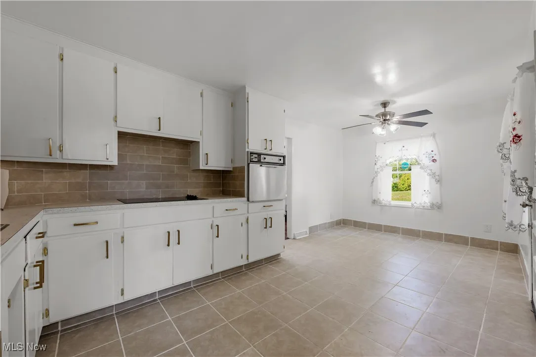 Kitchen featuring decorative backsplash, white cabinets, stainless steel oven, light tile patterned flooring, and light countertops