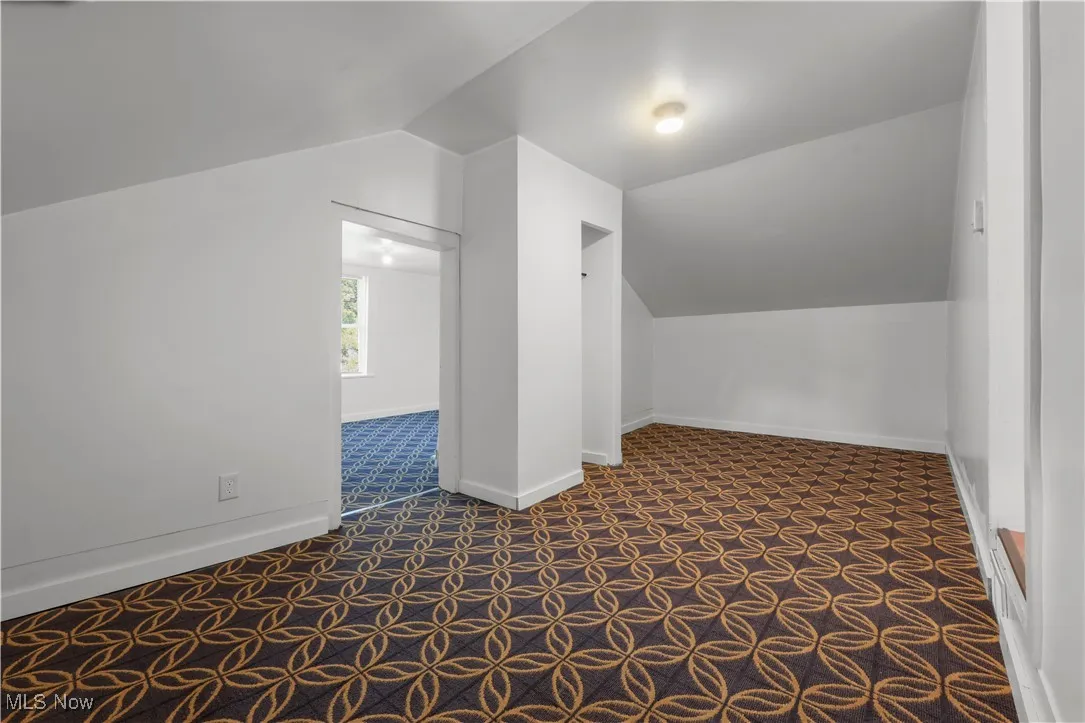Additional living space with dark colored carpet and vaulted ceiling