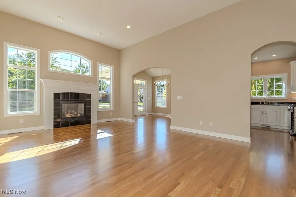 Unfurnished living room featuring light wood-style floors, arched walkways, recessed lighting, a tile fireplace, and a chandelier