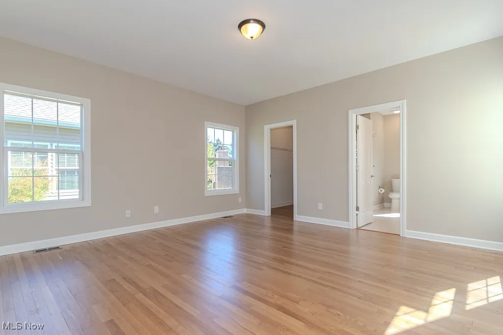 Unfurnished bedroom with a walk in closet, light wood-type flooring, and ensuite bathroom