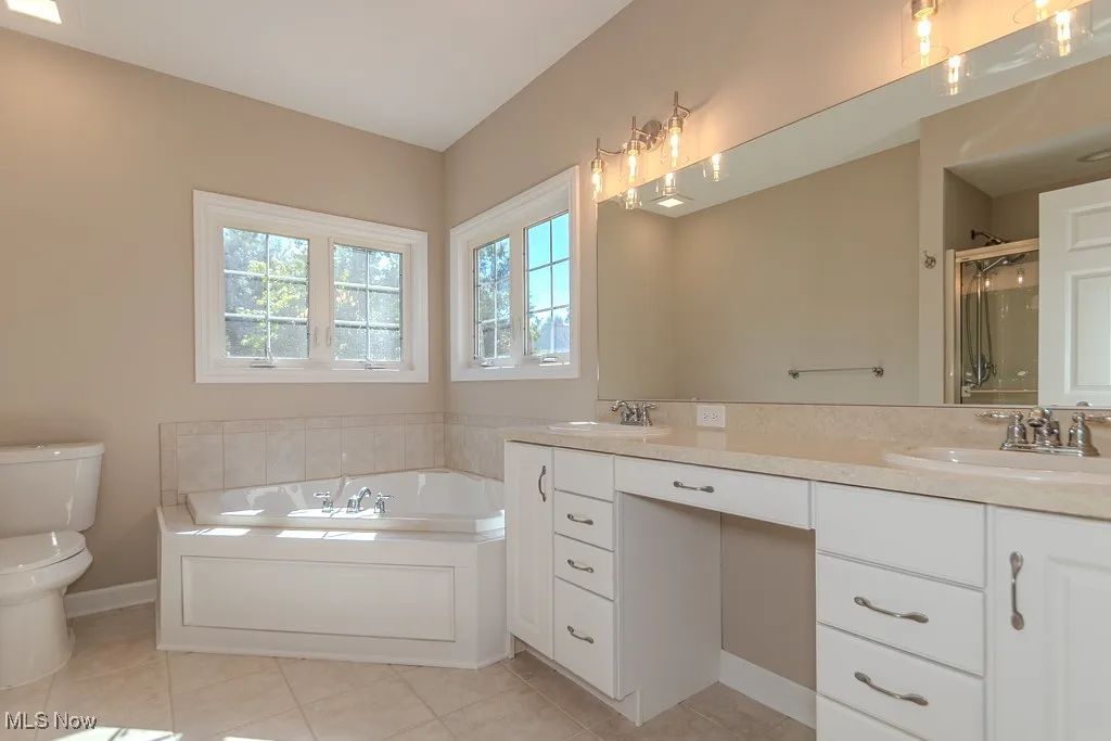 Full bath featuring double vanity, a garden tub, light tile patterned flooring, and a stall shower