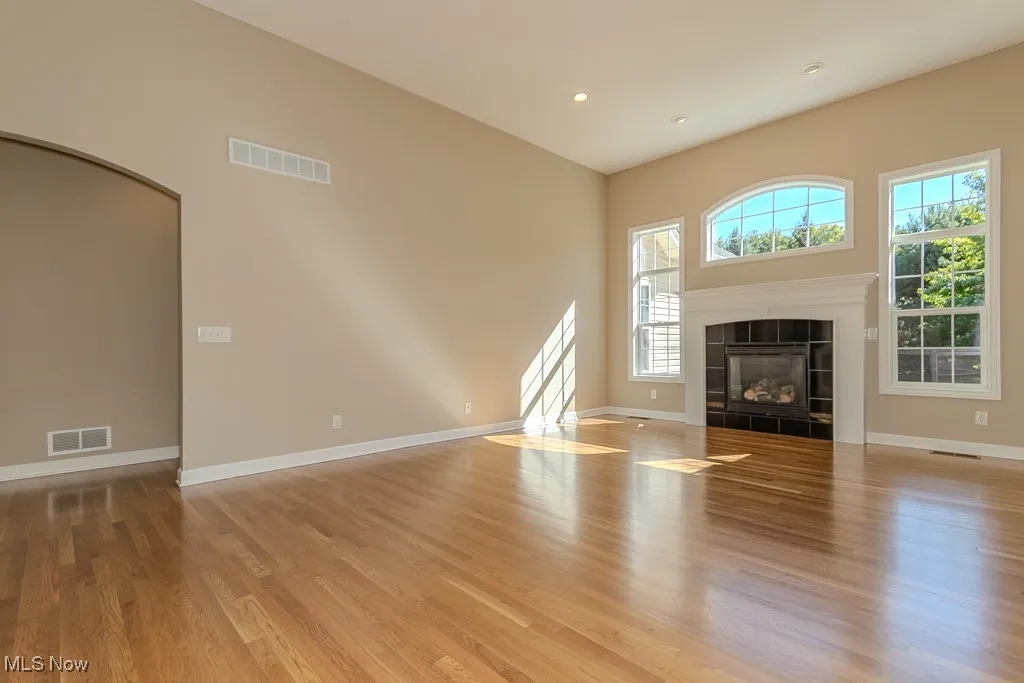 Unfurnished living room featuring light wood-style flooring, arched walkways, recessed lighting, a tile fireplace, and a high ceiling