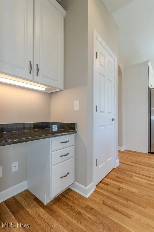 Kitchen with white cabinets, dark stone countertops, and light wood-style flooring