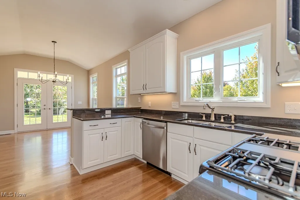 Kitchen with white cabinets, lofted ceiling, dishwasher, decorative light fixtures, and light wood-style flooring