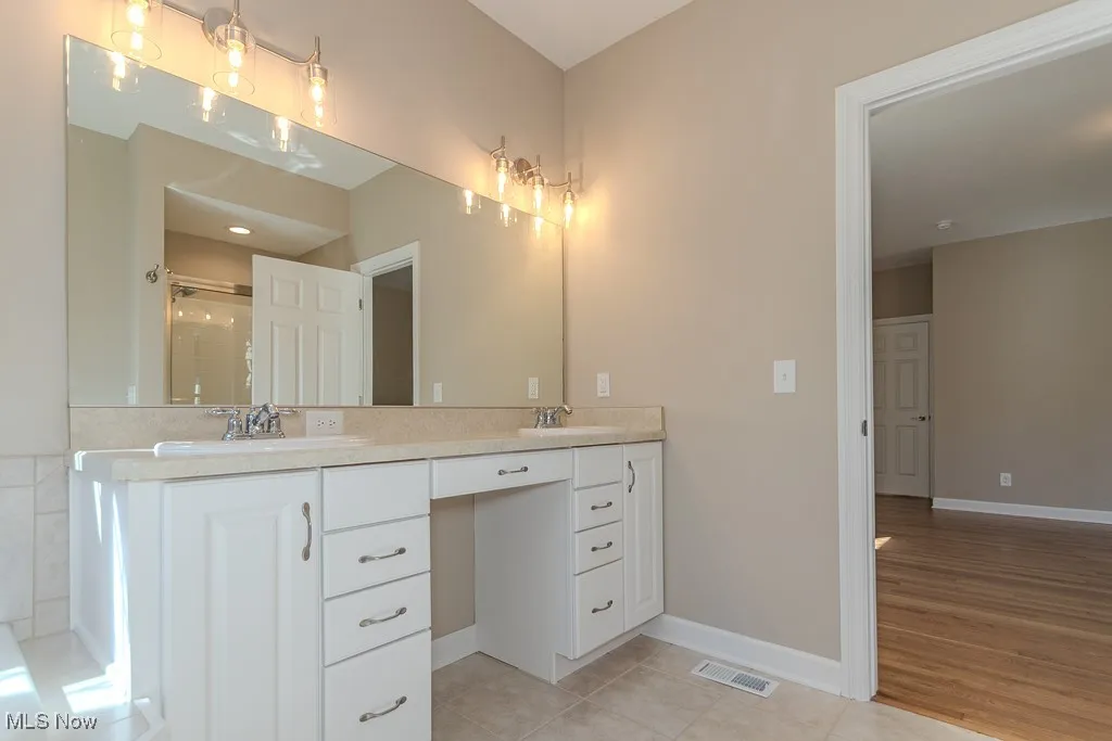 Full bathroom featuring double vanity, light tile patterned floors, and a stall shower