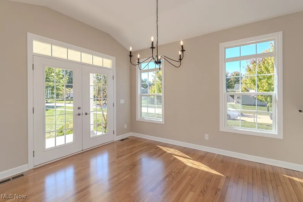 Doorway to outside featuring plenty of natural light, hardwood / wood-style flooring, lofted ceiling, a chandelier, and french doors