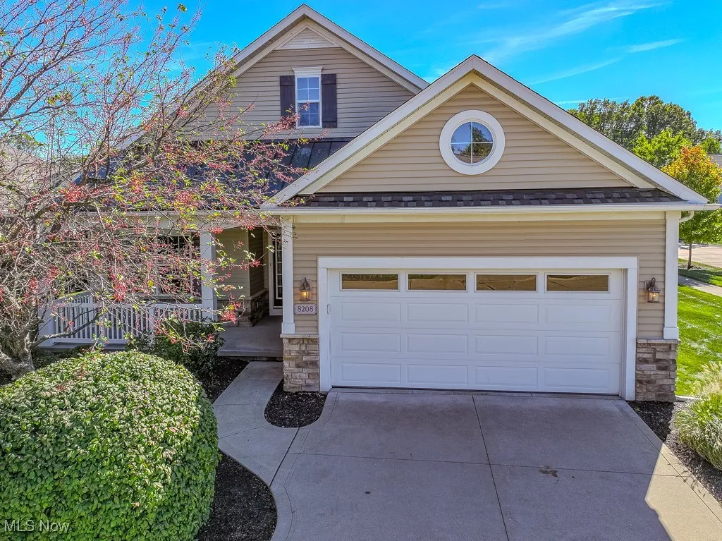 View of front of house with stone siding, concrete driveway, a shingled roof, covered porch, and an attached garage