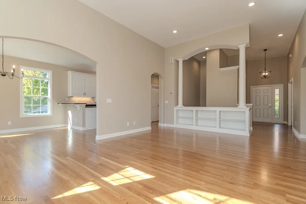 Unfurnished living room with a chandelier, arched walkways, light wood-style floors, recessed lighting, and a towering ceiling