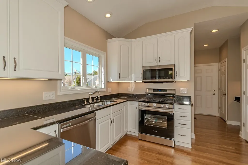 Kitchen with stainless steel appliances, white cabinets, vaulted ceiling, recessed lighting, and light wood-style floors