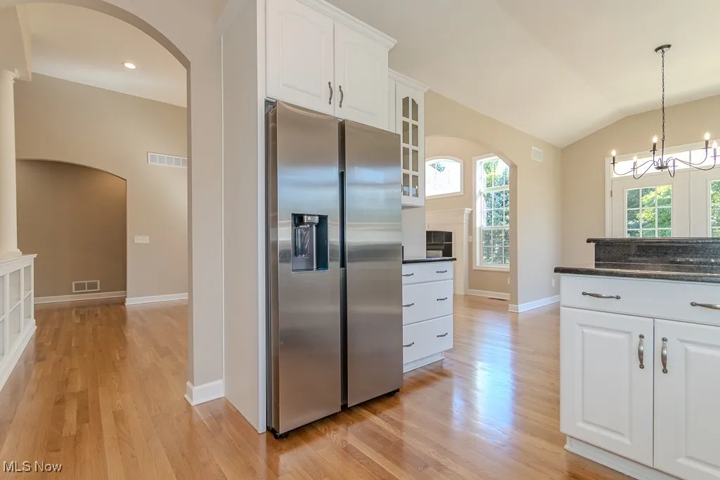 Kitchen with arched walkways, stainless steel refrigerator with ice dispenser, white cabinetry, pendant lighting, and dark stone counters