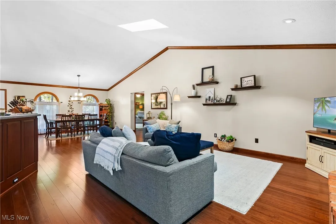 Living room with lofted ceiling, ornamental molding, dark wood-style flooring, and a skylight