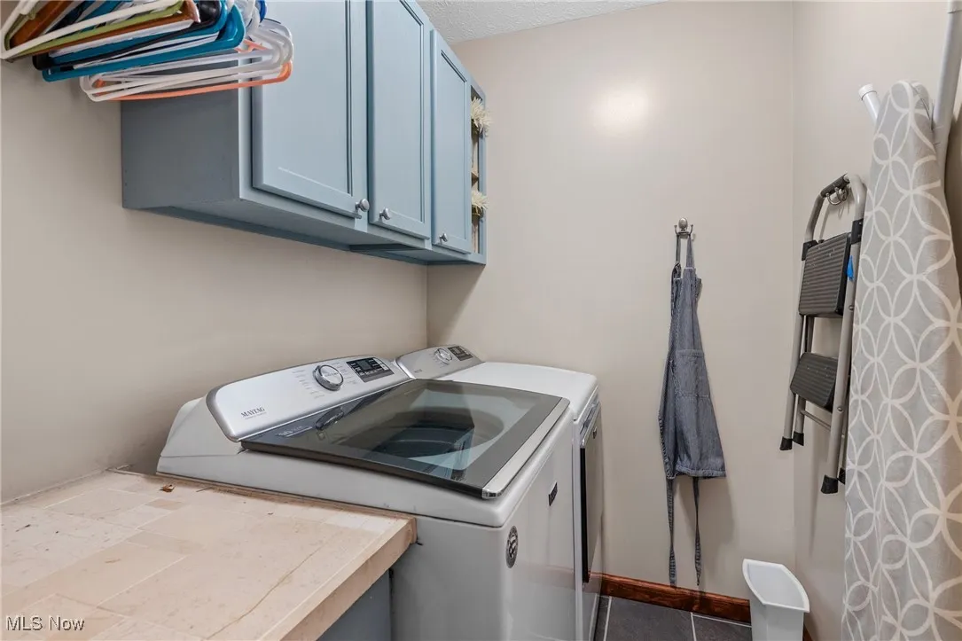 Laundry area featuring washing machine and clothes dryer, cabinet space, and dark tile patterned floors