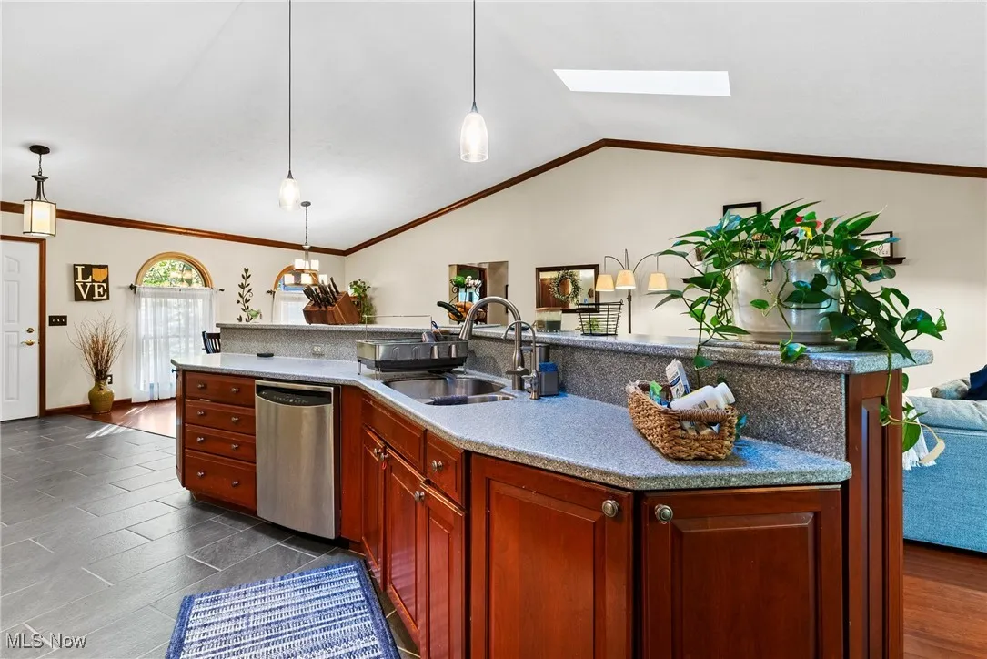 Kitchen featuring open floor plan, a skylight, stainless steel dishwasher, hanging light fixtures, and a kitchen island with sink