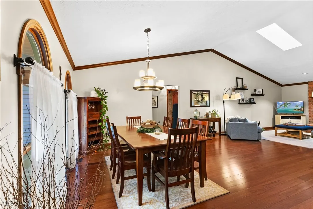 Dining area featuring ornamental molding, a skylight, lofted ceiling, dark wood-type flooring, and a chandelier