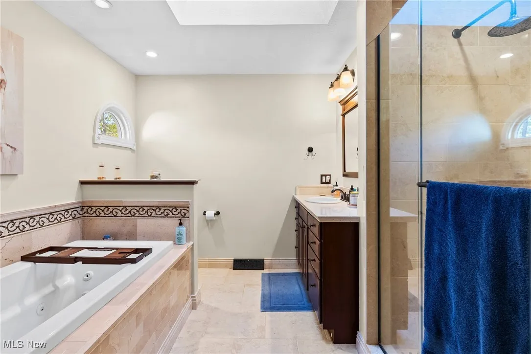 Bathroom featuring vanity, a skylight, a stall shower, a jetted tub, and light tile patterned flooring