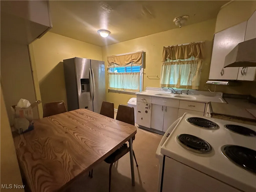 Kitchen featuring stainless steel fridge, electric range, white cabinets, light countertops, and exhaust hood