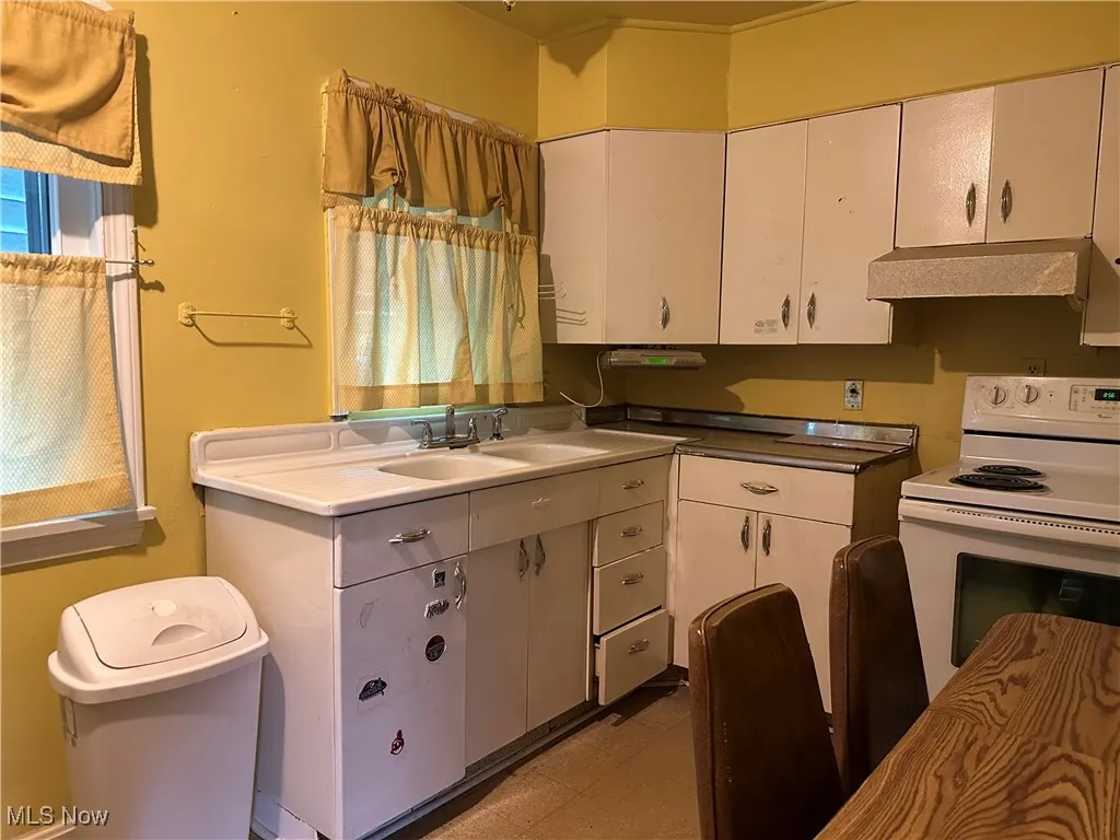 Kitchen featuring white electric stove, white cabinets, and premium range hood