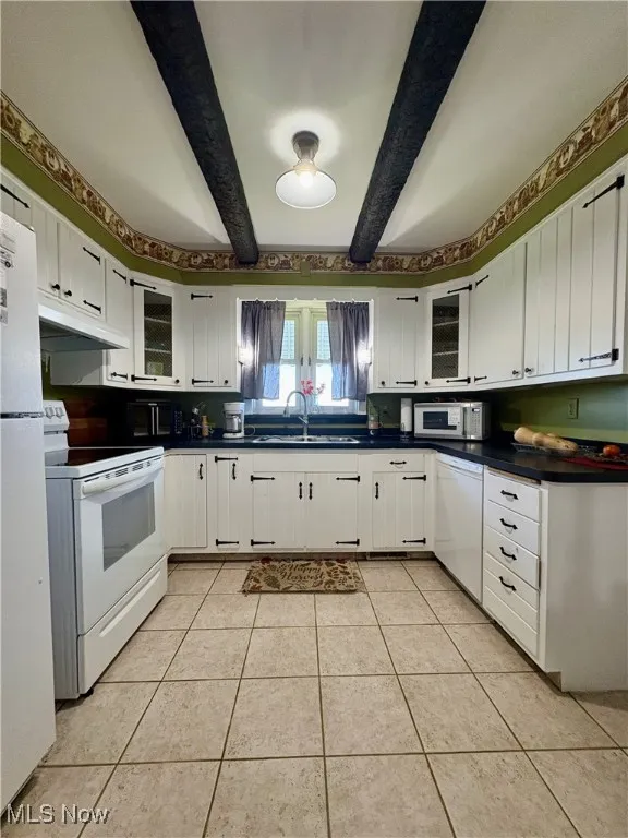 Kitchen featuring white cabinetry, white appliances, dark countertops, and beam ceiling