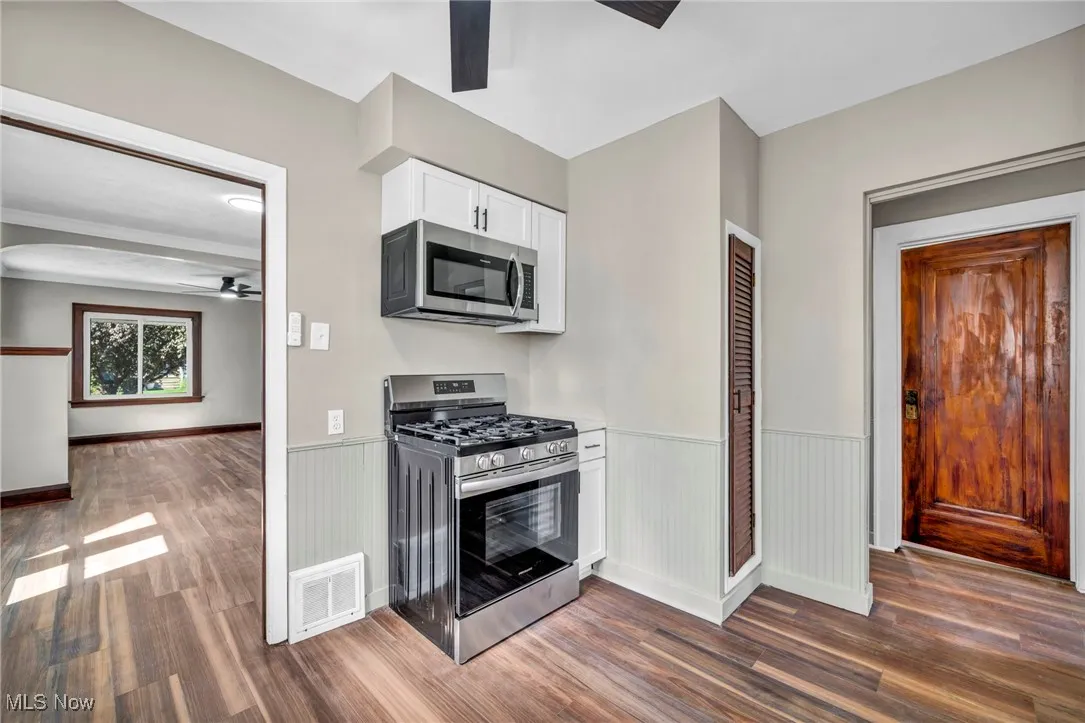 Kitchen featuring a ceiling fan, stainless steel appliances, white cabinets, and dark wood-type flooring