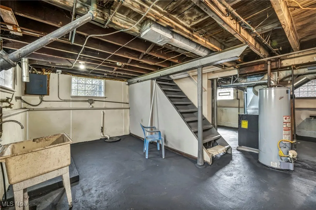 Below grade area featuring plenty of natural light, water heater, stairs, and electric panel