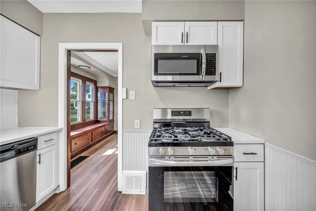 Kitchen featuring appliances with stainless steel finishes, white cabinetry, wainscoting, dark wood-type flooring, and light stone countertops