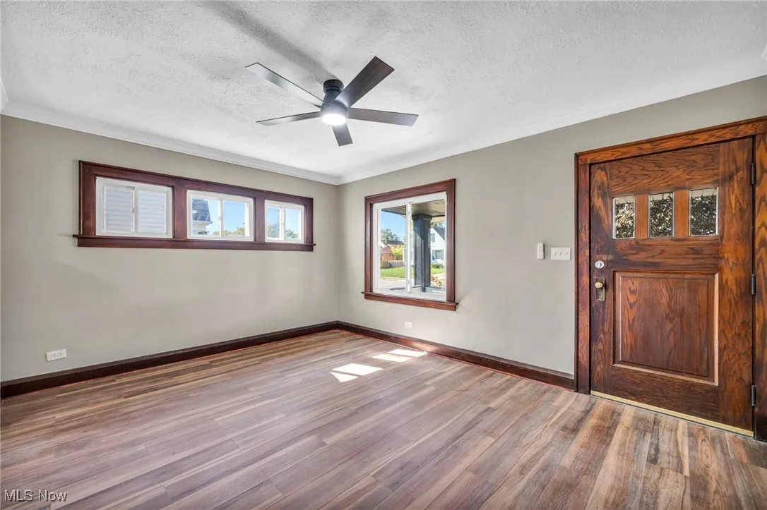 Entryway with wood finished floors, a textured ceiling, a ceiling fan, and crown molding