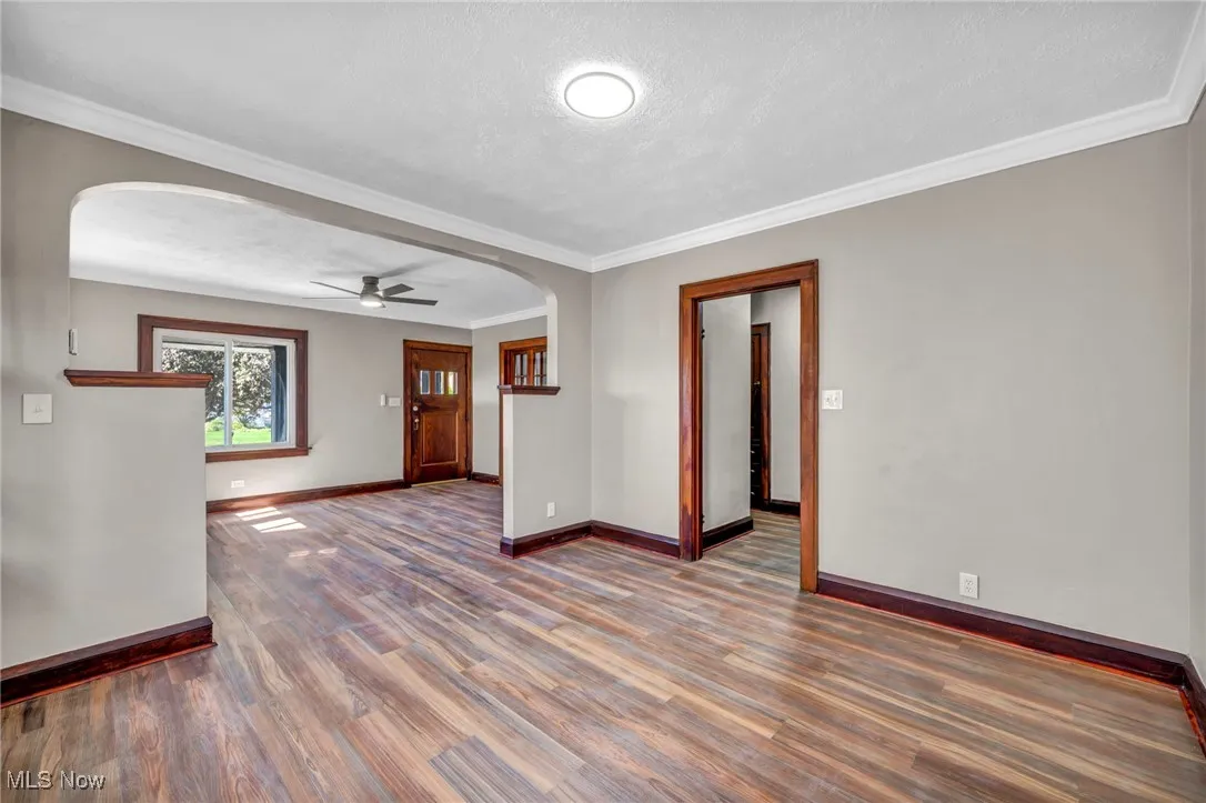 Unfurnished room featuring arched walkways, ornamental molding, dark wood finished floors, ceiling fan, and a textured ceiling