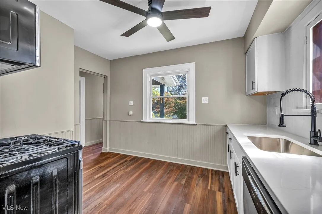 Kitchen featuring wainscoting, light stone countertops, dark wood-style floors, appliances with stainless steel finishes, and white cabinetry