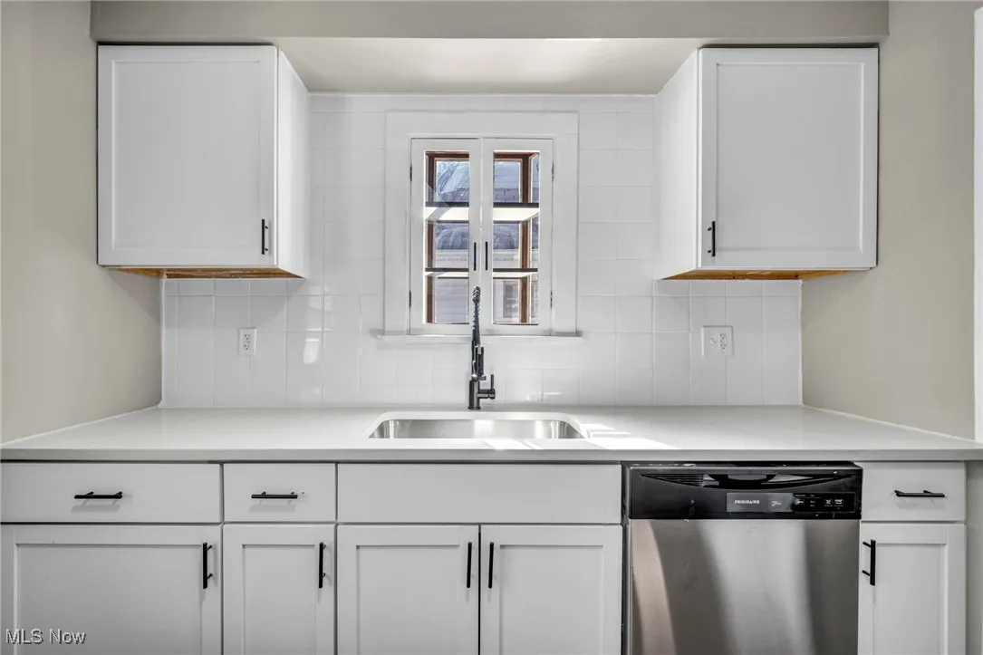 Kitchen with white cabinetry, dishwasher, tasteful backsplash, and light stone counters