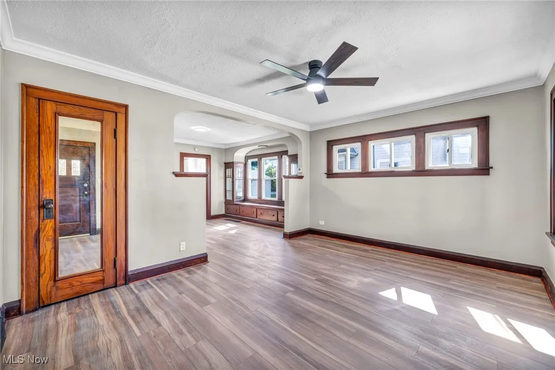 Empty room featuring arched walkways, ornamental molding, wood finished floors, a textured ceiling, and ceiling fan