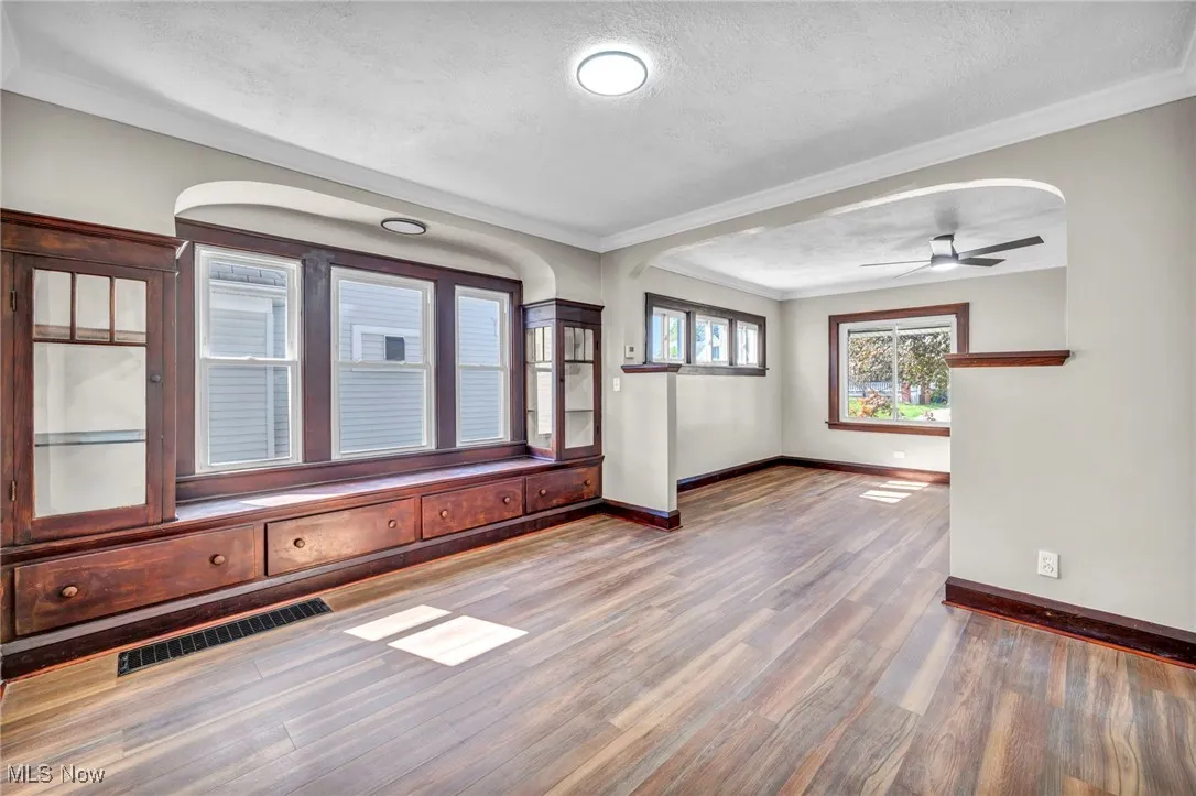 Unfurnished room with crown molding, a textured ceiling, wood finished floors, a ceiling fan, and arched walkways